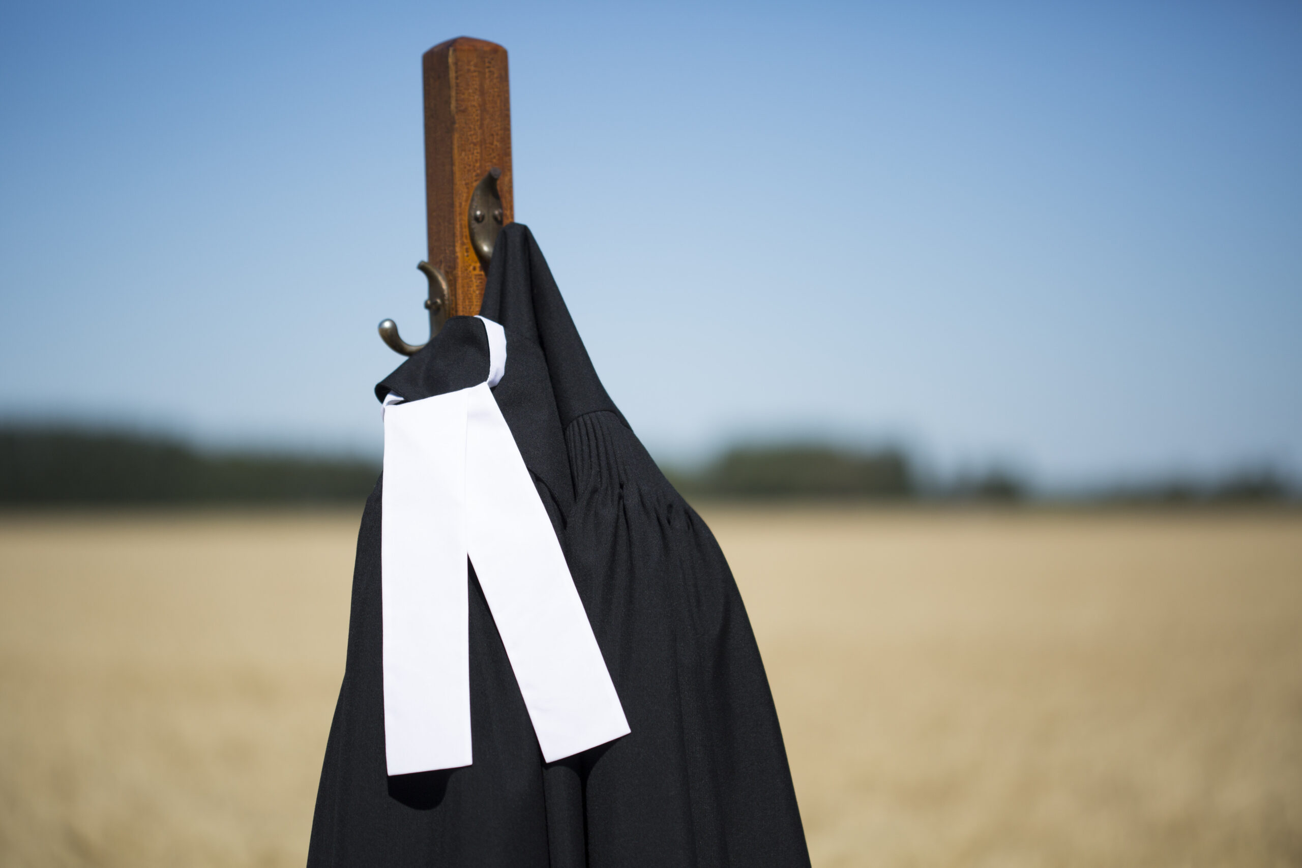 A black robe draped over a wooden post, set against a grassy field under a clear sky.